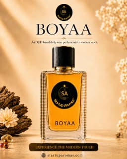 Boyaa luxury daily wear perfume bottle by Startup Aromas, elegantly presented on a golden textured surface with soft background lighting, flanked by a delicate white flower and dry floral accents.